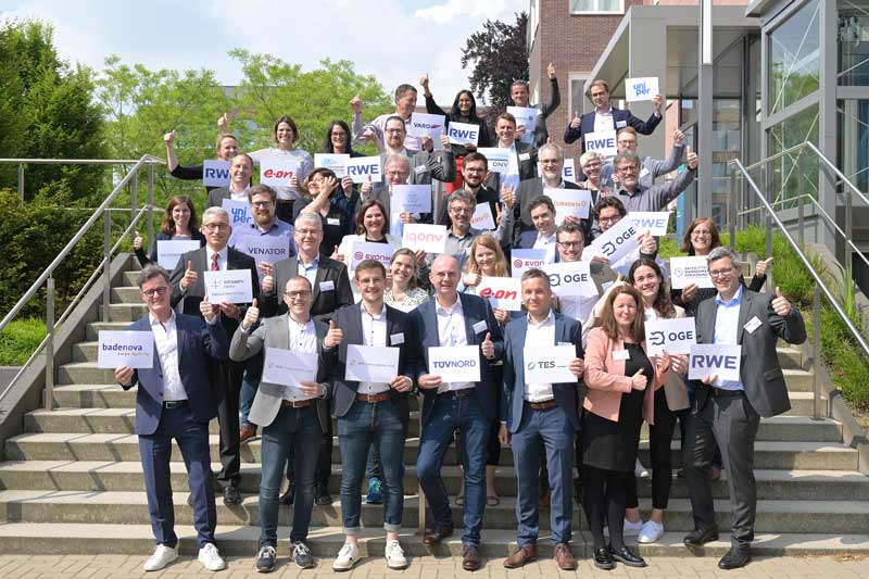 A group of people poses on stairs while holding signs with various company names.